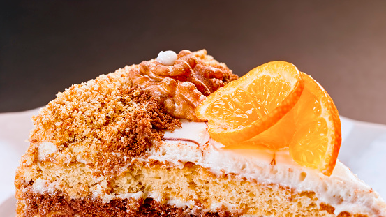 Close-up of slice of walnut cake topped with walnut and orange slice served on plate.