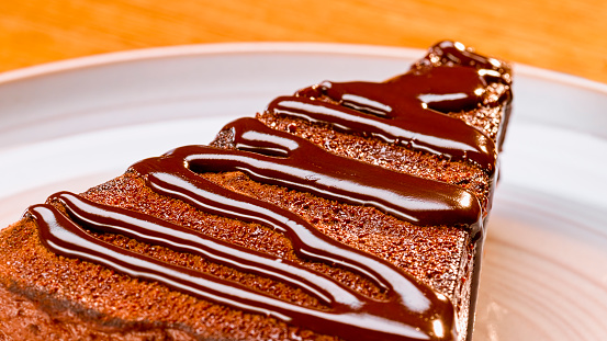 Close-up of slice of chocolate cake with brown fudge sauce served on plate.