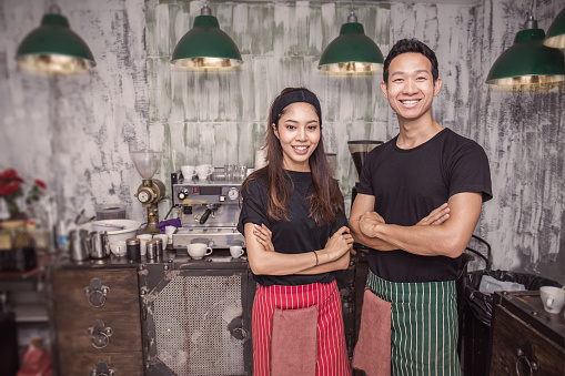 Startup successful small business owner man and woman standing with arms crossed in his coffee shop or restaurant. Portrait of young asian tan couple barista cafe owner. Small business entrepreneur together teamwork concept.