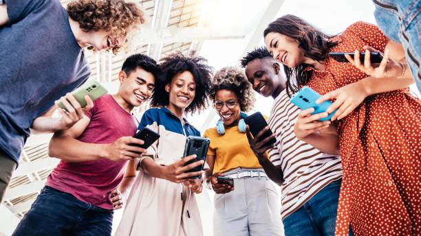 Diverse teenage students using digital smart phones mobile at college campus - Group of friends watching cellphones sharing content on social media platform - Youth, friendship and technology concept stock photo