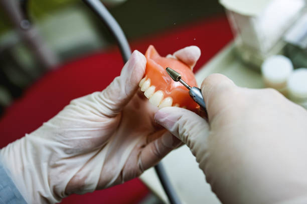 primo piano di un odontotecnico che modella un dente di protesi con uno strumento alla scrivania. - laboratory dentures dental hygiene human teeth foto e immagini stock