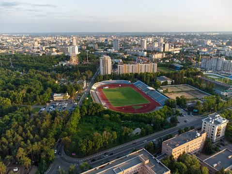 Drone view of Kharkiv city center near Park of Maxim Gorky, stadium and residential multistory buildings with scenic sunset cloudy sky in summer