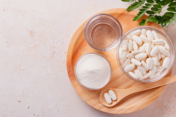 Collagen powder, pills and glass of water on wooden tray, top view Collagen powder, glass of water and collagen pills on neutral beige background. Collagen supplements in different forms for beautiful and young skin, copy space collagen stock pictures, royalty-free photos & images