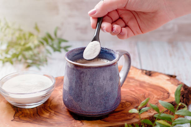 frau, die kollagenpulver zu ihrem morgenkaffee hinzufügt. beauty collagen ergänzung, zusätzliche kollagenaufnahme - gemahlen stock-fotos und bilder