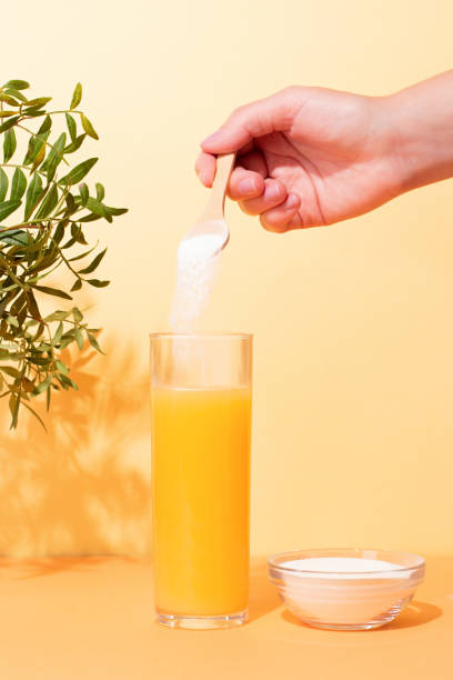 mujer que agrega colágeno en polvo al jugo de naranja sobre un fondo colorido - juice plus fotografías e imágenes de stock