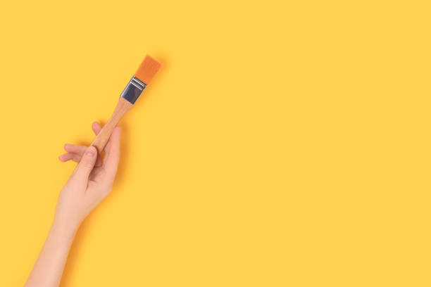 istock Female hand hold paintbrush on a yellow background. 1328678701