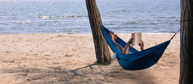 man reading a book in a hammock by the sea