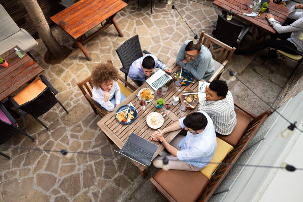 Top view of a multi-ethnic business people having a meeting over lunch in a restaurant outdoors Top view of a small group of multi-ethnic diverse people discussing business over a lunch in a restaurant outdoors. business dinner stock pictures, royalty-free photos & images