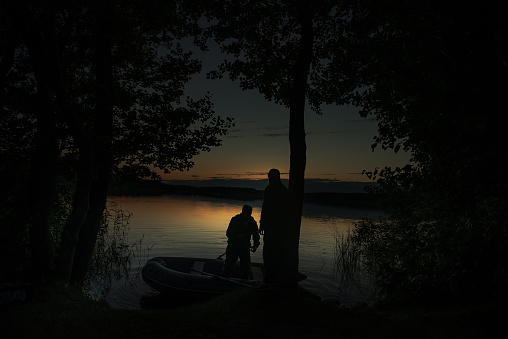 night fishing. boats moored to the shore of the night lake, father and son are returning from fishing. silhouettes. night shooting, soft selective focusing