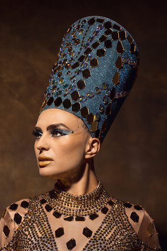 Elegance. Close-up beautiful young woman in image of Nefertiti in art performance isolated on brown vintage background. Female model like famous queen of Egypt. Comparison of eras concept.