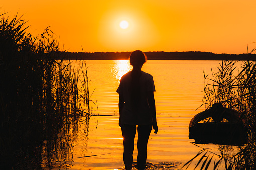 Silhouette of woman walking to the beautiful lake during bright orange summer warm sunrise