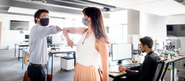 istock Young businesspeople in protective masks elbow bumping in an office 1328689528