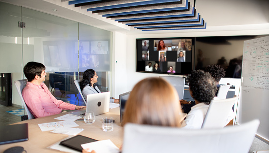 Diverse group of businesspeople sitting around table in an office boardroom during a video conference with remote staff on monitors