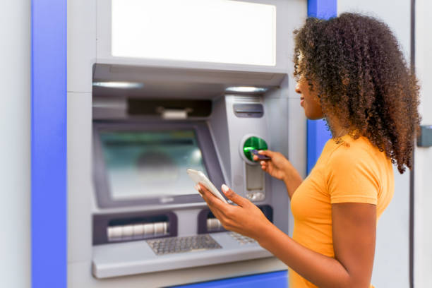 one black woman withdrawing money at an atm - atm imagens e fotografias de stock
