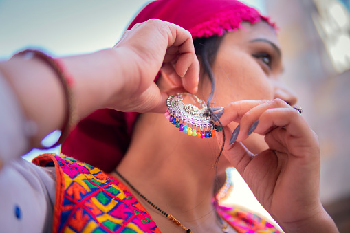 Low angle close-up image of beautiful traditional Indian young woman puts on earrings.