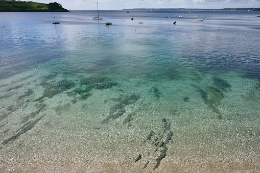 Scenic views over the shallow clear sea at St. Mawes, Cornwall towards the mouth of the River Fal on a sunny June day.