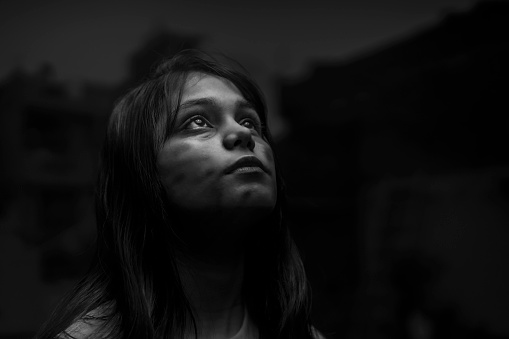 Monochrome  Indian portrait of a poor teenager girl looking up side and praying god. very poor girl. scars on face.