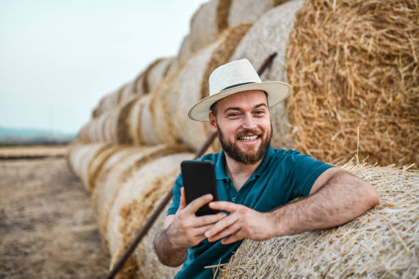 agricoltore sorridente barbuto che si fa selfie mentre organizza balle di fieno sul campo - hay wheat bale stacking foto e immagini stock