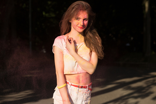 Delightful young woman posing covered with yellow and pink Holi paint