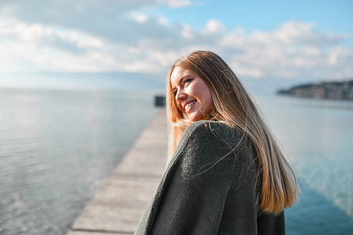 Smiling Blond Female Enjoying Autumn Sun By The Lake