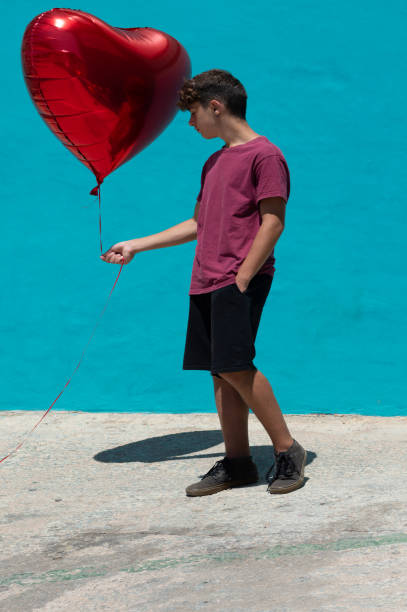 istock handsome boy pensive while holding a red heart-shaped helium balloon in his hand 1328705280