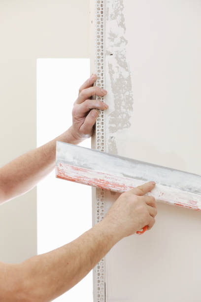 istock Builder in protective mask using a trowel to add plaster. Plastering wall with putty-knife, close up image. Fixing wall surface and preparation for painting. construction work during quarantine 1328707388