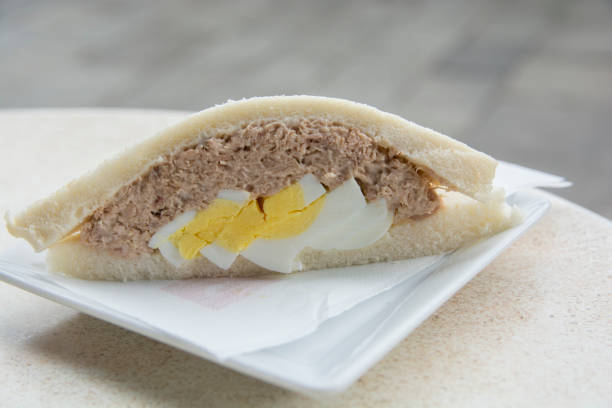 Close up of a Tramezzino, a triangular Italian sandwich constructed from two slices of soft white bread, with the crusts removed, containing hard boiled egg and tuna fish stock photo