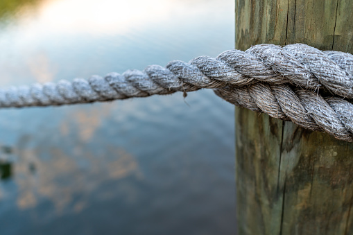 Wooden post and rope railing on a dock with the reflection of clouds on the lake, shot with a shallow depth of view to have the background out of focus.