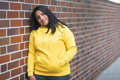 Latino girl with a yellow hoodie in front if a brick wall