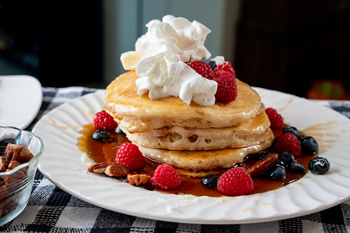 Fluffy Pancakes with syrup whipped cream raspberry and blueberry on a white plate