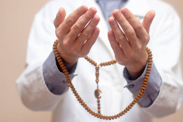 istock A young man in a white robe raised his hands up and prayed with a Muslim rosary. Beige background. Doctor praying. A Muslim makes dua. 1328724419