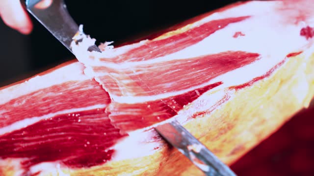 Anonymous person cutting a 100% Iberian ham leg and holding with tweezers an appetizing and delicious slice of Iberian ham. Acorn-fed Iberian Ham. Typical Spanish or Catalan food. Iberian pork meat.