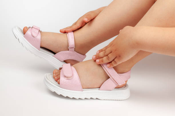 macro detalles sandalias rosas para niños en los pies de la niña de un niño sentado sobre un fondo blanco vertido - shoe single object isolated red fotografías e imágenes de stock
