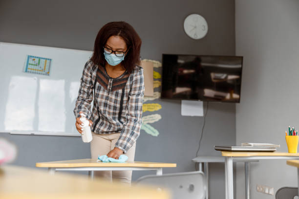 istock Teacher holding disinfectant and standing in classroom 1328727323