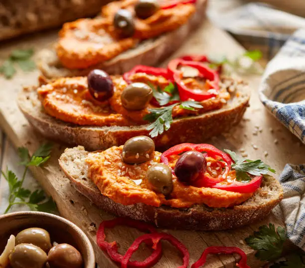 Close up view of a sandwich with sourdough bread with addition of  paprika hummus, olives, slices of red pepper and herbs close up view. Vegetarian food concept
