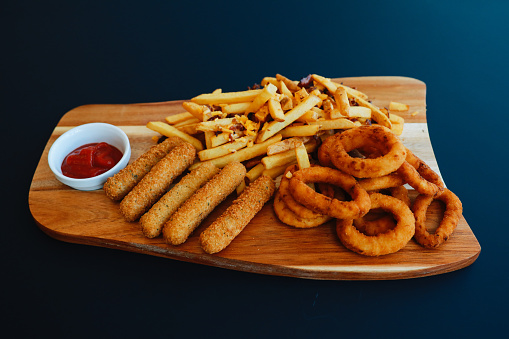 Onion rings and mozzarella sticks with french fries on the table in the restaurant.