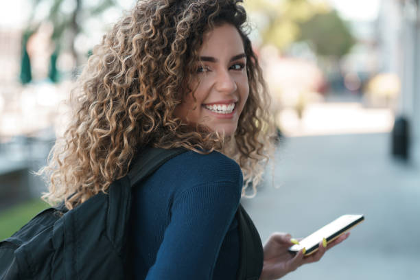 istock Latin woman smiling while using a mobile phone outdoors on the street. 1328739113