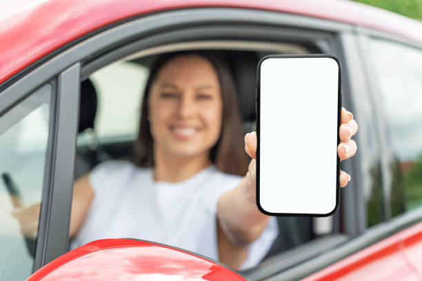 istock Young woman driving a car shows a smartphone screen. 1328741639