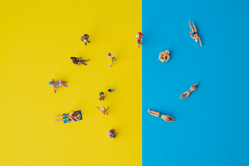 miniature people on yellow and blue paper, holiday situation with swimming or sunbathing people