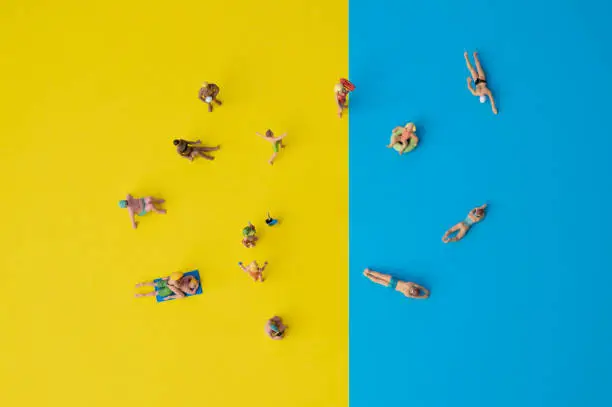 Photo of miniature people on yellow and blue paper, holiday situation with swimming or sunbathing people