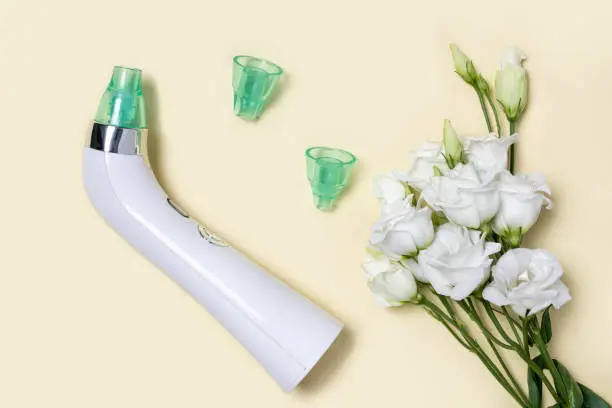 Photo of Blackhead vacuum remover or pore cleaner is home beauty and skin care device for facial cleaning. Tender white flowers Eustoma on pastel yellow background