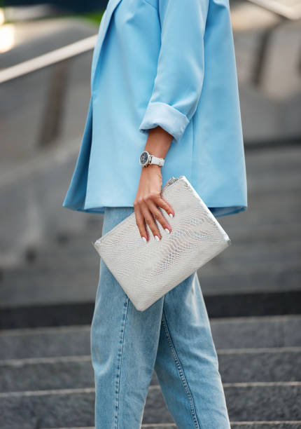 Women's silver clutch bag with snakeskin texture. A fragment of the body of a model in a summer blue blazer with rolled-up sleeves and blue jeans. Business style clothing. older woman purse stock pictures, royalty-free photos & images
