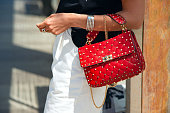 A bright red leather handbag with iron spikes hangs on a woman's hand.