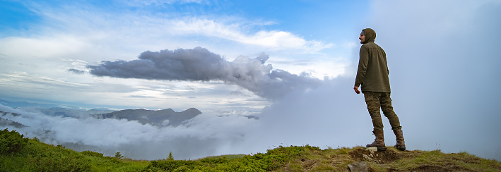 The man standing on the mountain on the white clouds background