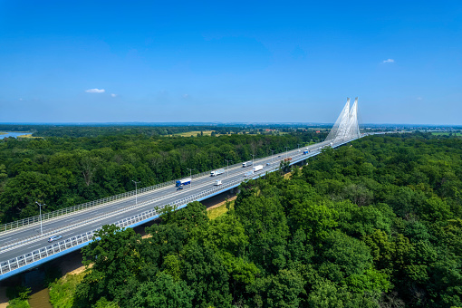 highway crossing the green forest with the cable-stayed bridge on a horizon