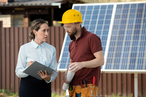 Serious female engineer explaining contractor where to install solar panels in backyard