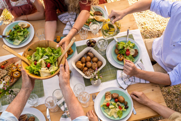 Vegan Dinner Party Hands of people eating baked potatoes, vegetable salad and grilled vegetables at family dinner family reunion stock pictures, royalty-free photos & images