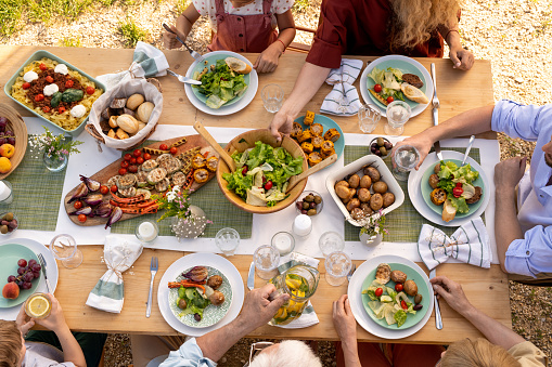 Group of people eating delicous food at festive dinner table with salad and grilled vegetables, view from the top