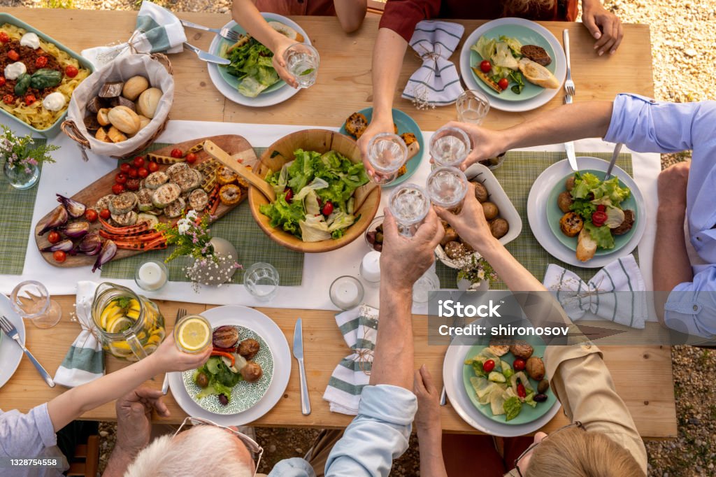 People Toasting with Glasses of Water Group of people toasting with glasses of fresh water over dinner table with tasty healthy food Healthy Eating Stock Photo