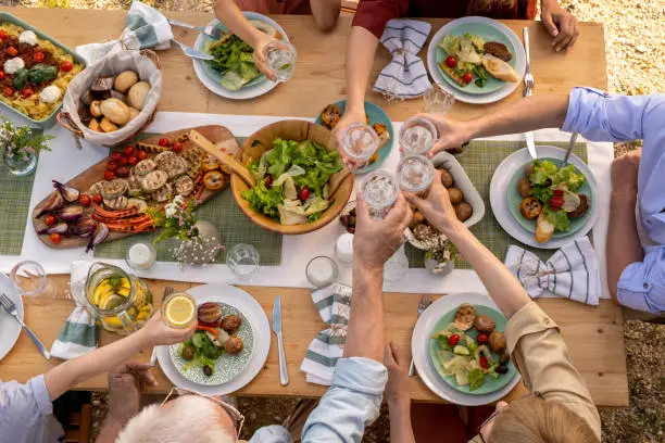 Group of people toasting with glasses of fresh water over dinner table with tasty healthy food